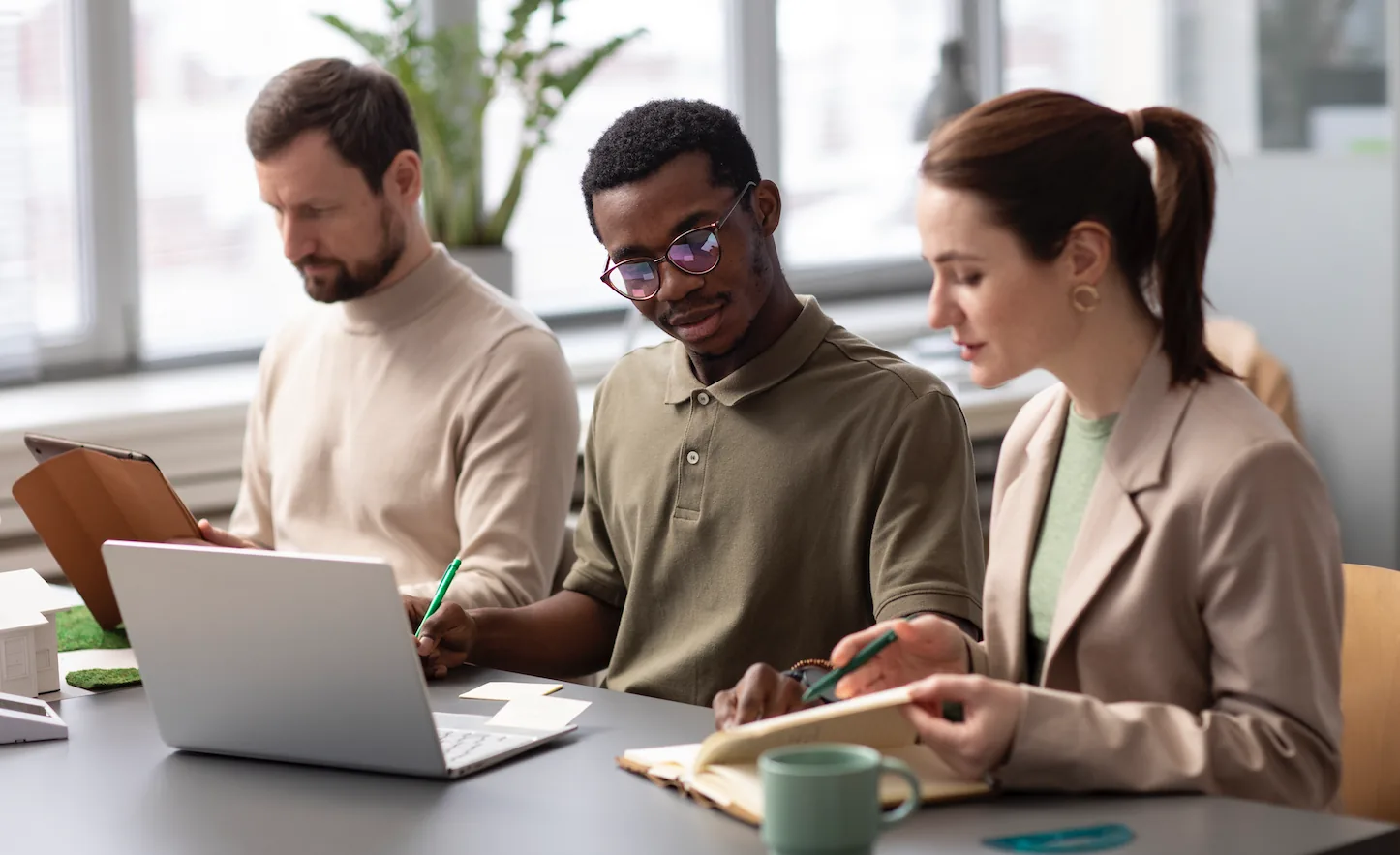 Equipe corporativa em treinamento, com laptop, tablet e anotações sobre a mesa